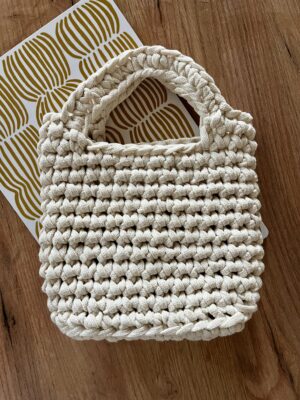 Valkoinen käsin virkattu tyylikäs laukku, jossa kahva.